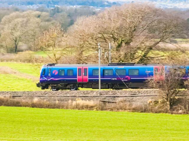The train moves swiftly on tracks surrounded by lush green grass and distant trees.