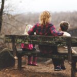 A woman sits on a bench with a child either side of her looking out at a landscape