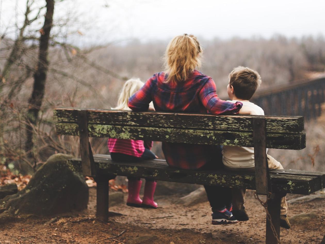 A woman sits on a bench with a child either side of her looking out at a landscape