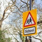 a school roadsign showing silhouettes of children crossing a road in a red triangle