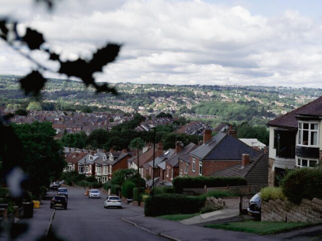 A view of a residential street lined with houses and greenery, leading down a hill.